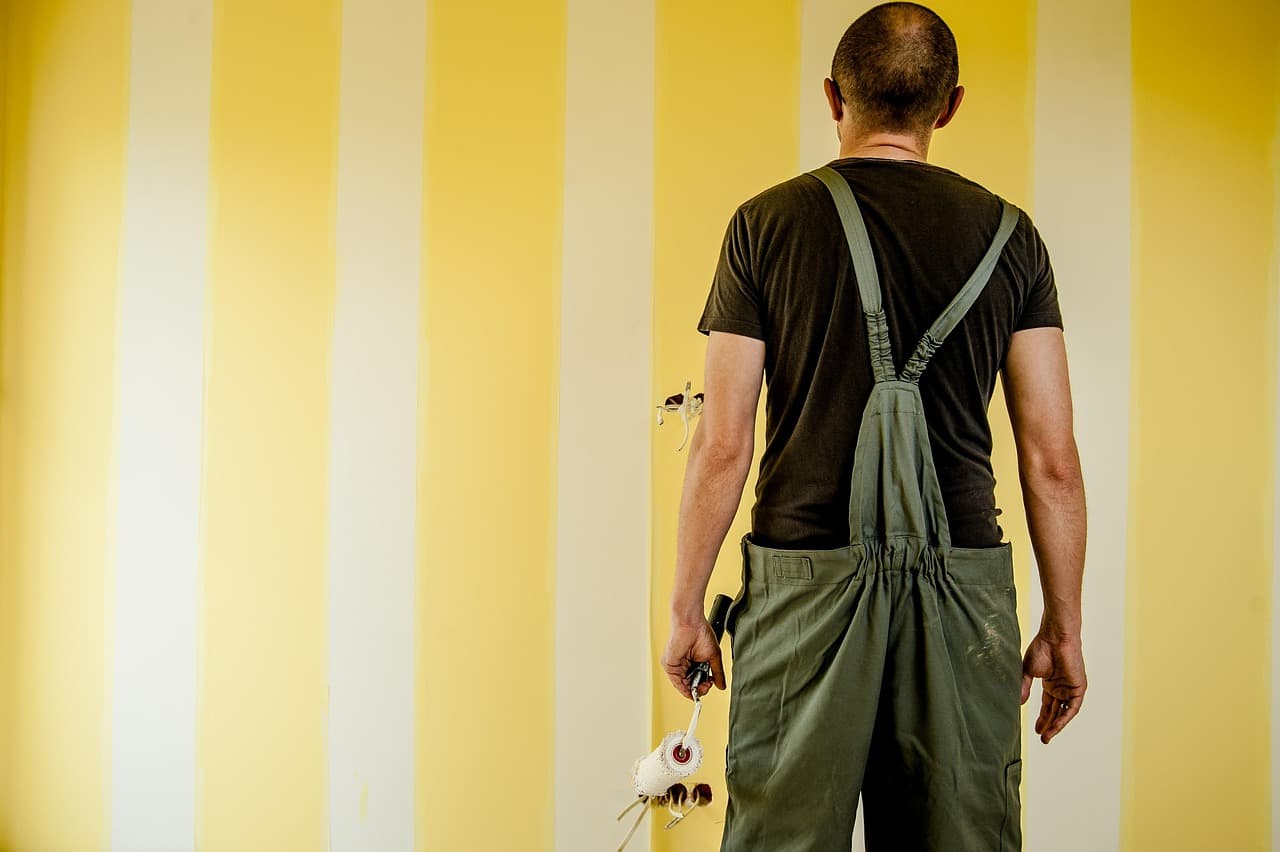 Decorator in bib overalls painting broad yellow and white stripes on a wall